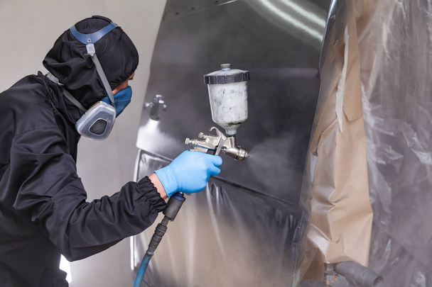 Een mannelijke werknemer in jumpsuit en blauwe handschoenen verven met een spray gu - Foto, afbeelding