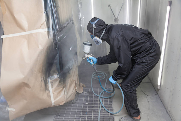 Een mannelijke werknemer in jumpsuit en blauwe handschoenen verven met een spray gu - Foto, afbeelding