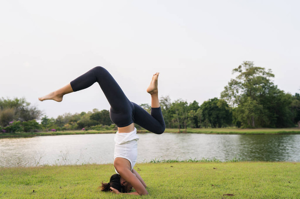 Молодая азиатка йога на открытом воздухе сохраняет спокойствие и медитирует, практикуя йогу, чтобы исследовать внутренний мир. Йога полезна для здоровья возле озера в парке. Концепция спорта и здорового образа жизни
. - Фото, изображение