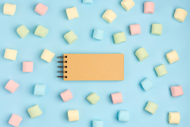 Blue paper background with marshmallow and notepad. Place for your text. Cozy sweet background - 写真・画像
