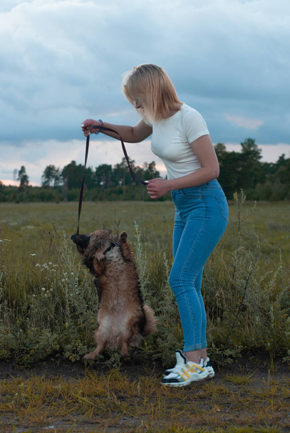 Retrato de una mujer feliz paseando con su mascota en un parque fuera de la ciudad, rubia con el perro posando
, - Foto, Imagen