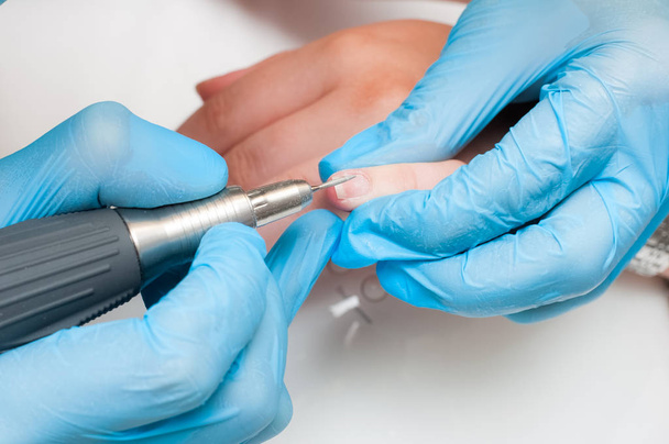 Vrouw gebruik elektrische nagel bestand drill in schoonheidssalon. Perfecte nagels manicure proces of operatie in close-up. - Foto, afbeelding