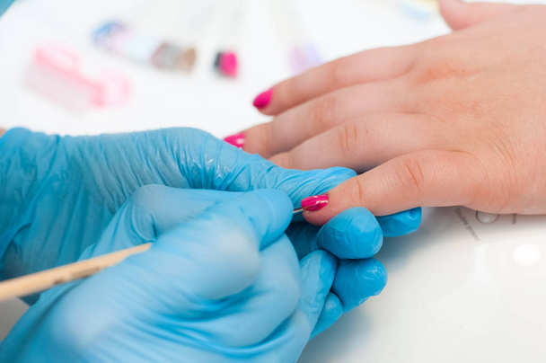 Manicure nail paint pink color. Nail care. Closeup of beautiful woman hands getting manicure in spa salon. Female manicurist cleaning cuticle with professional manicure. Cosmetic procedure. - 写真・画像