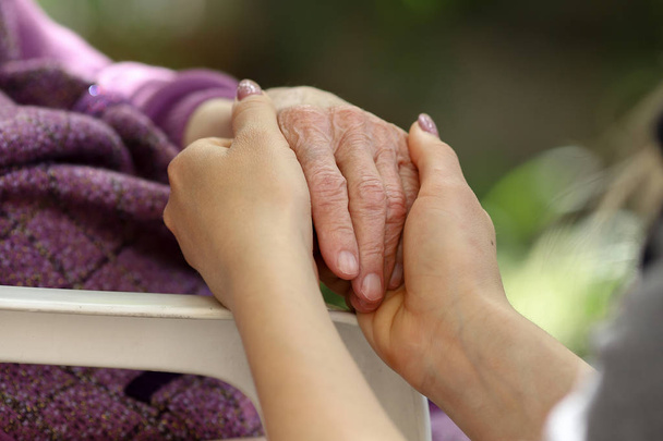 Hands of young adult and senior women. Senior and young holding hands outside. Elderly concept - Photo, Image