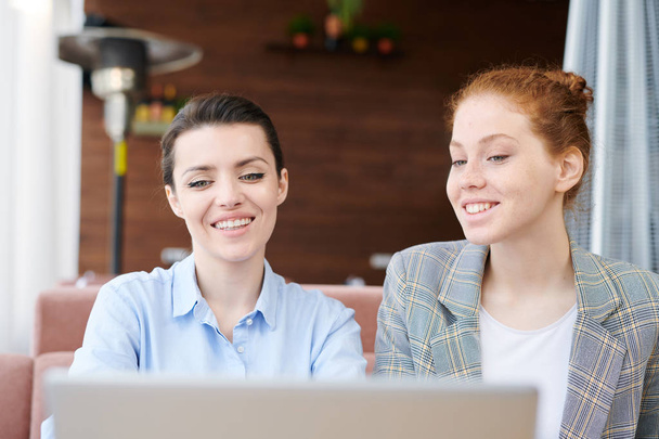 Cheerful positive young businesswomen satisfied with survey results using modern laptop while discussing project plan - 写真・画像
