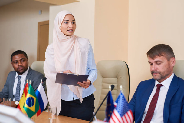 Jovem mulher muçulmana no hijab fazendo relatório na conferência enquanto estava em frente ao público no salão
 - Foto, Imagem