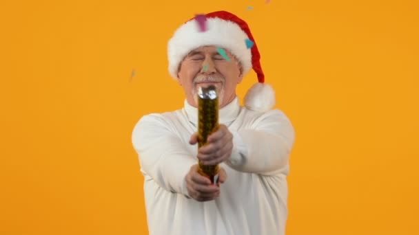 Senior male blowing up confetti firecracker orange background, party decoration - Imágenes, Vídeo