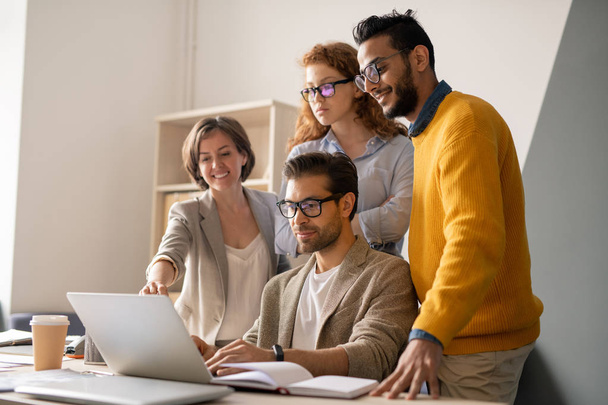 Група молодих багатоетнічних бізнес-фахівців, які дивляться на екран ноутбука та аналізують презентацію разом в офісі
 - Фото, зображення