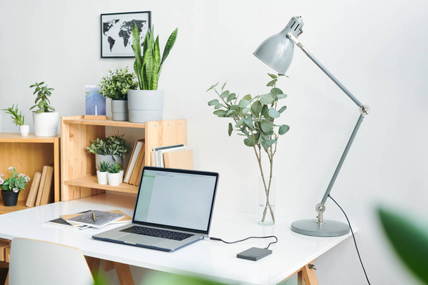 Local de trabalho com laptop, lâmpada, livros, livros, prateleiras de madeira e plantas domésticas verdes em vasos de flores e imagem do mapa na parede
 - Foto, Imagem