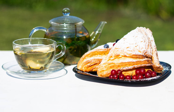 Heerlijk ontbijt met verse croissants en rijpe bessen en muntthee op de achtergrond van groen gras. Zomer ontbijt tijd. - Foto, afbeelding