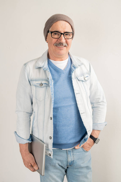 Uomo maturo casual in jeans blu e pullover, giacca bianca, occhiali e berretto in piedi davanti alla telecamera su sfondo bianco
 - Foto, immagini