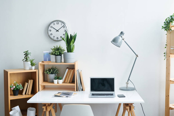 Nykyaikaisen toimistotyöntekijän työpaikka, jossa on kirjoituspöytä, lamppu, oppikirjat, hyllyt, joissa on kirjoja ja kasveja, vempaimia ja kello seinällä
 - Valokuva, kuva