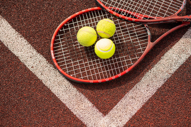 白線を横切って横たわる2つのテニスラケットと3つの黄色いボールのトップビュー - 写真・画像