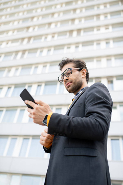 Giovane uomo d'affari serio con gadget lettura messaggio o notifica in ambiente urbano da edificio moderno
 - Foto, immagini