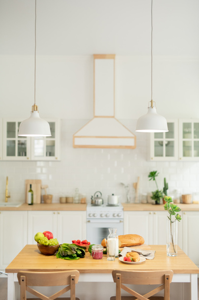 Interieur van de keuken in moderne flat of huis met keukengerei en lampen opknoping over tafel met groenten en zelfgemaakte gerechten - Foto, afbeelding
