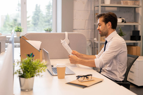 Sérieux jeune employé de bureau en chemise blanche concentré sur la paperasserie assis au bureau et travaillant avec des données
 - Photo, image