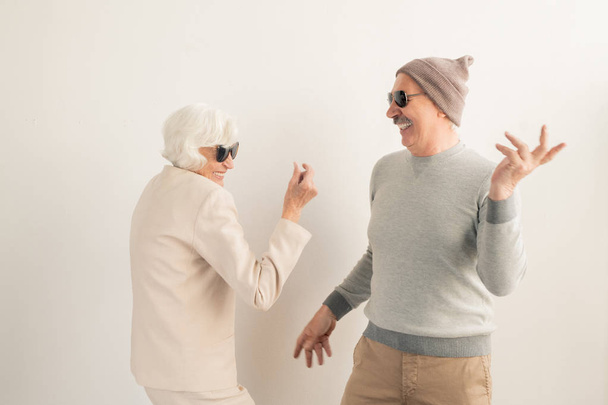 Heureux couple de personnes âgées occasionnelles en lunettes de soleil s'amuser et danser en isolement sur fond blanc
 - Photo, image