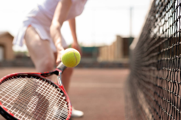 Tennisball über Schläger, gehalten von einer jungen Spielerin, die ihn fängt oder wirft - Foto, Bild