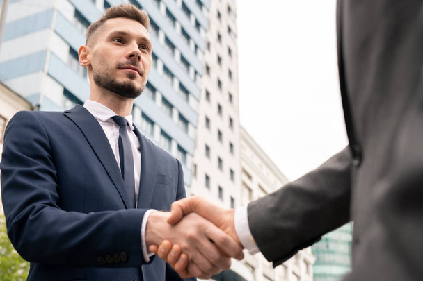 Jeune homme d'affaires élégant serrant la main du client après avoir négocié et signé un contrat lors d'une réunion en plein air
 - Photo, image