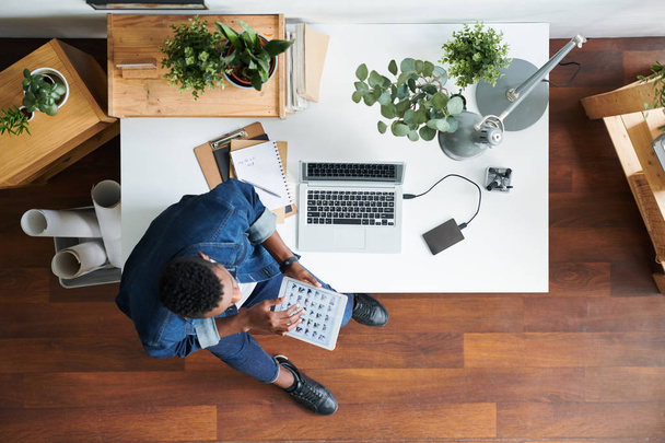 Вид молодого современного сотрудника в повседневной одежде, сидящего за письменным столом и думающего о новых идеях для отчета в офисе
 - Фото, изображение