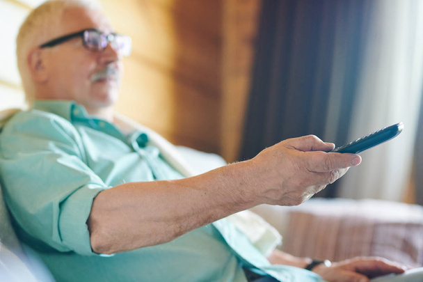 Käsi nykyajan rento vanhempi mies ohjaa kaukosäädin televisiossa vaihtaessaan kanavia
 - Valokuva, kuva