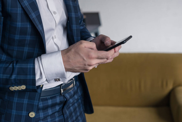 close-up of a man who holds in his hand a smartphone . He is standing im loft interior . business person browsing internet or connecting to wireless via touchscreen pad - Photo, Image