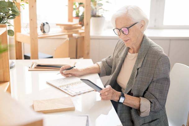 Сучасна старша мобільна добре одягнена жінка в окулярах, яка читає сповіщення в смартфоні під час роботи в офісі
 - Фото, зображення