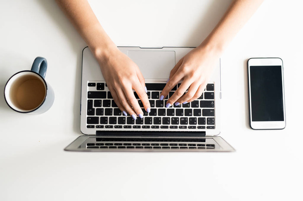 Молоді жіночі руки над клавіатурою ноутбука, що входить в дані, оточені мобільним гаджетом і гарячим чаєм в кухоль
 - Фото, зображення