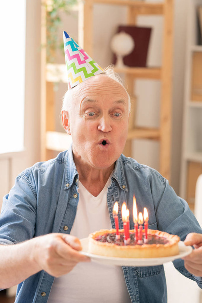 Öregember fúj gyertyák házi születésnapi torta, miközben egyedül ünnepli - Fotó, kép