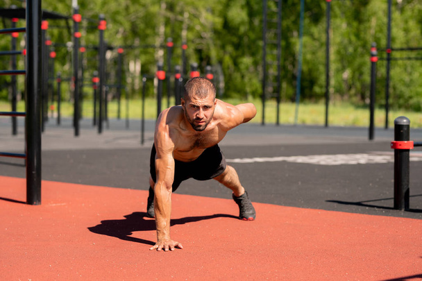 Musculoso jovem fisiculturista inclinado nos pés e na mão direita, enquanto estirando o braço esquerdo para trás durante o exercício
 - Foto, Imagem