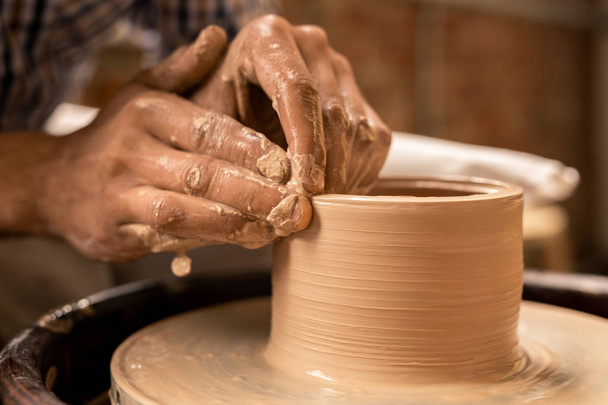 Ręce rzemieślnej trzymając obracający się przedmiot glinianego garnka podczas pracy przez koło garncarskie w warsztacie - Zdjęcie, obraz