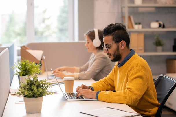 Концентрированный молодой арабский менеджер с бородой сидит за столом с коллегой и использует ноутбук во время работы над планом продаж
 - Фото, изображение