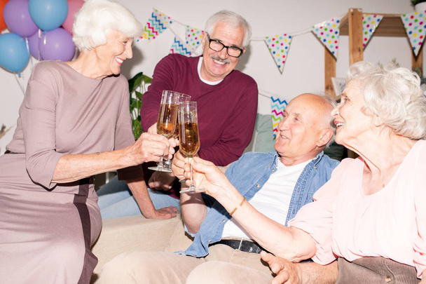 Cheerful amigável idosos clinking com flautas de champanhe enquanto se diverte na festa em casa
 - Foto, Imagem