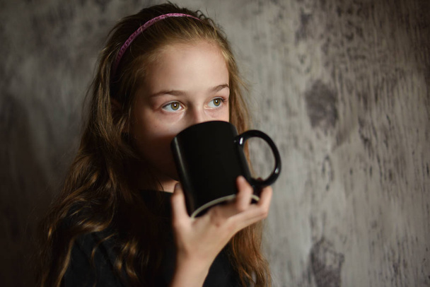 Маленька дівчинка тримає чашку кави в чорній футболці. Макет, ідеально підходить для розміщення вашого дизайну
. - Фото, зображення