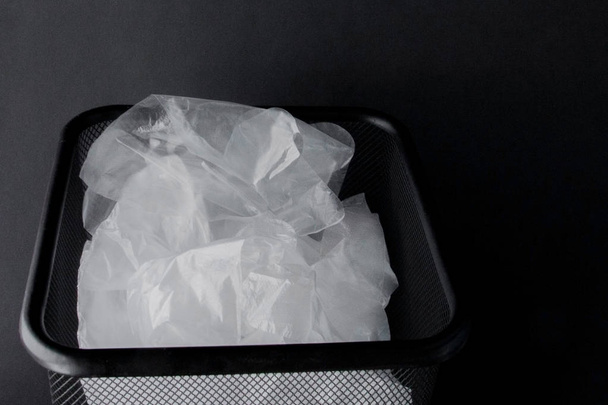 Plastic bag with handles, gloves in the bin on a black background . Used plastic bag for recycling. Concept - ecology, planet pollution with plastic cellophane polyethylene - 写真・画像
