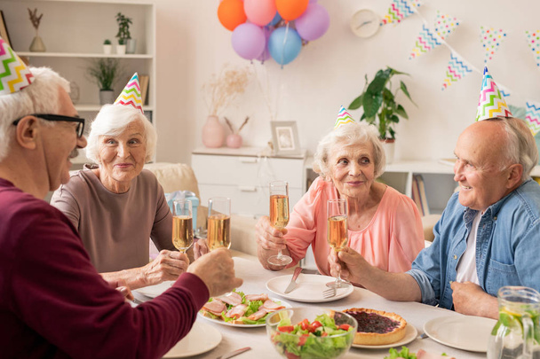 Grupo de pessoas idosas sentadas à mesa servida em casa enquanto comemoram o aniversário
 - Foto, Imagem