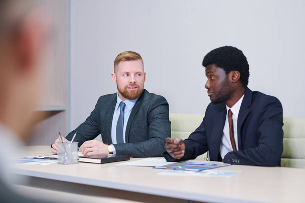 Kaksi nuorta kulttuurienvälistä liikemiestä keskustelee työasioista ja ideoista tapaamisessa
 - Valokuva, kuva