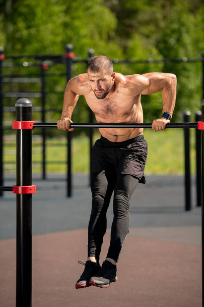Jeune athlète musculaire se penchant sur la barre de sport tout en suspendant au-dessus du sol pendant l'exercice physique
 - Photo, image