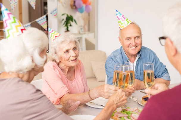 Gruppe fröhlicher Senioren klingelt mit Sektflöten am servierten Tisch - Foto, Bild