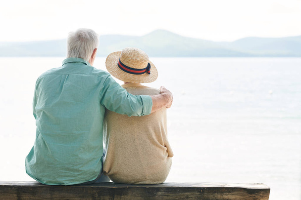 Vista posteriore di coppia anziana serena in casualwear guardando il lago mentre si rilassa sul lungomare durante la giornata estiva
 - Foto, immagini