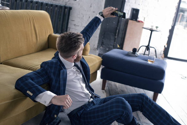 Udostępnianie zdjęć. Przystojny młody człowiek w pełny garnitur biorąc selfie siedząc na podłodze w domu - Zdjęcie, obraz