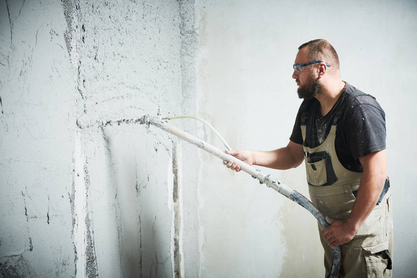 Plasterer using screeder spraying putty plaster mortar on wall - Foto, imagen
