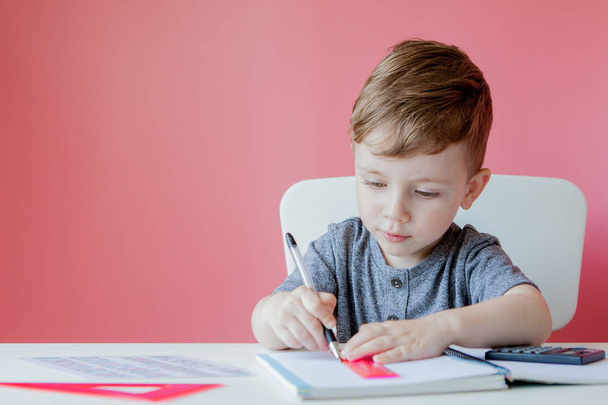 Portrait of cute kid boy at home making homework. Little concentrated child writing with colorful pencil, indoors. Elementary school and education. Kid learning writing letters and numbers - Фото, изображение