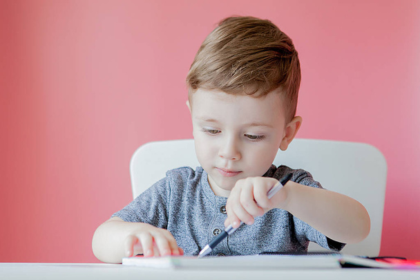Portrait of cute kid boy at home making homework. Little concentrated child writing with colorful pencil, indoors. Elementary school and education. Kid learning writing letters and numbers - Photo, image