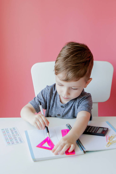 Portrait of cute kid boy at home making homework. Little concentrated child writing with colorful pencil, indoors. Elementary school and education. Kid learning writing letters and numbers - Photo, image