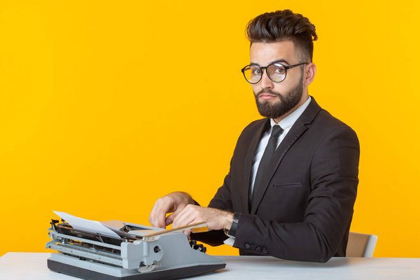 Jonge knappe mannelijke zakenman in formele kleren typen van tekst op een schrijfmachine poseren op een gele achtergrond. Plaats voor reclame. Business concept. - Foto, afbeelding
