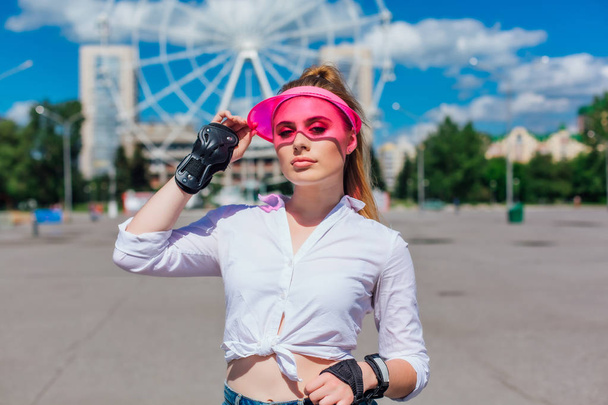 Portrait of an emotional girl in a pink cap visor and protective gloves for rollerblades and skateboarding. - Foto, afbeelding