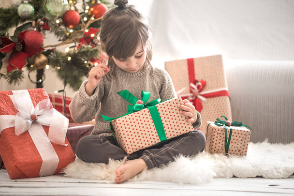 Kaunis pieni tyttö pitelee lahjapakkausta ja hymyilee istuessaan
 - Valokuva, kuva