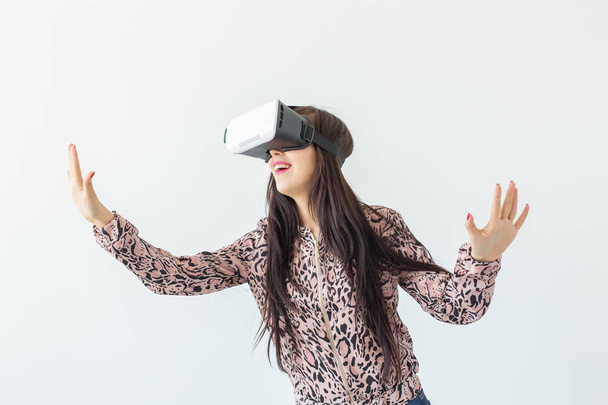 Young woman watches a movie with glasses of virtual reality standing on a white background. The concept of new features and modern technology - 写真・画像