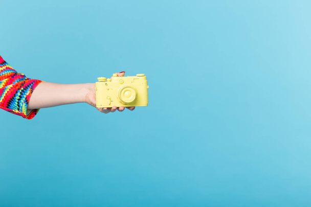 Fotografie und Vintage-Konzept - weibliche Hand mit gelber Retro-Kamera auf blauem Hintergrund mit Kopierraum - Foto, Bild
